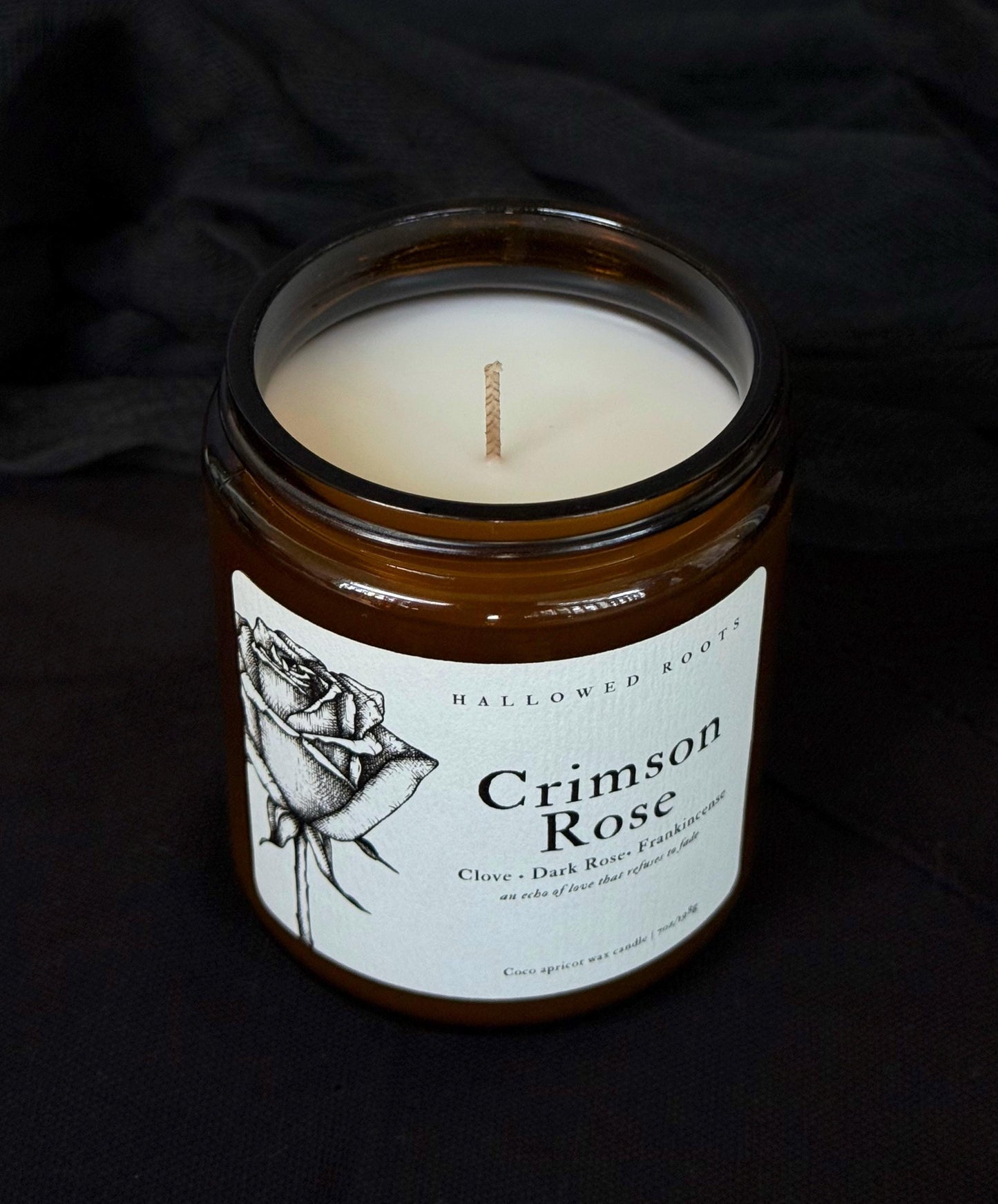 Candle in a jar labeled 'Crimson Rose' on a dark background