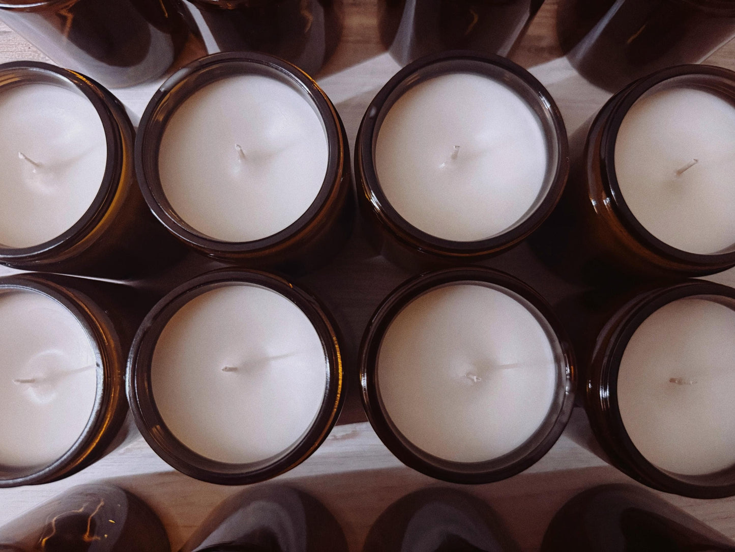 White candles in brown holders arranged in a grid on a wooden surface.