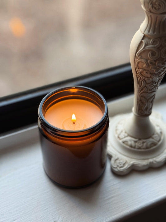 Candle in an amber jar with a white decorative candle holder on a windowsill.