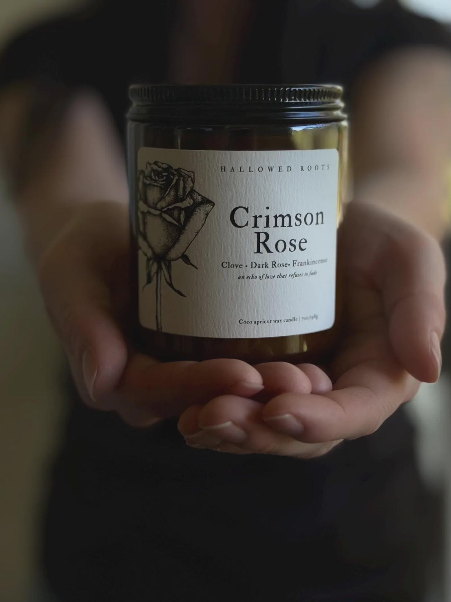 Jar of 'Crimson Rose' candle held in hands with a blurred background