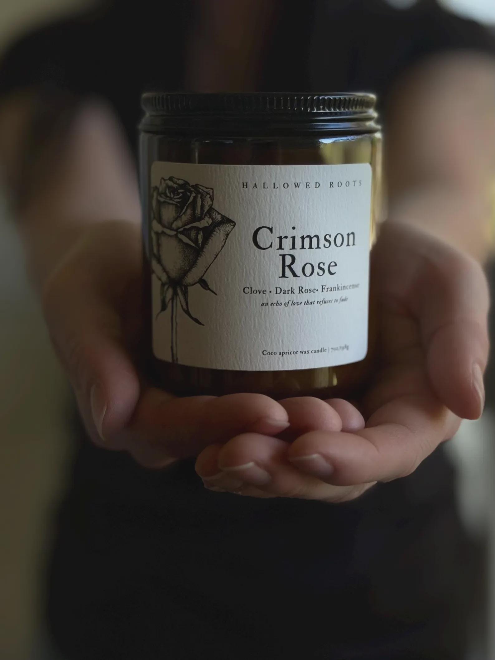 Jar of 'Crimson Rose' candle held in hands with a blurred background