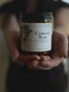 Jar of 'Crimson Rose' candle held in hands with a blurred background